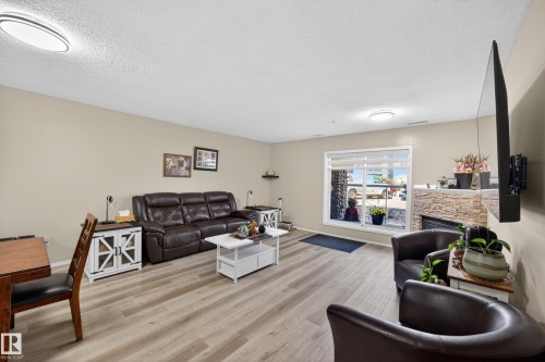 Living area featuring wood-finish flooring, neutral wall tones, and a stone-clad fireplace with hearth - 138 16035 132 Street, Edmonton, AB 