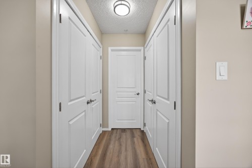 Hallway with wood-finish flooring, light tan wall color, and white trim - 138 16035 132 Street, Edmonton, AB 