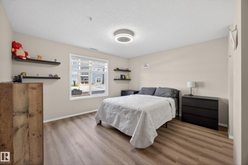Spacious room featuring wood-finish flooring, light neutral wall tones, and a large window with white trim - 138 16035 132 Street, Edmonton, AB 