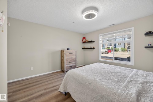 Spacious room featuring wood-finish flooring, a large window with white framing, and a modern ceiling light fixture - 138 16035 132 Street, Edmonton, AB 