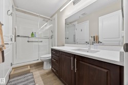 Spacious bathroom featuring a glass-enclosed shower with white subway tile, a dark wood-finish vanity with a light-toned countertop, a rectangular undermount sink, and a large mirror - 