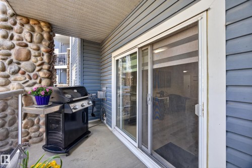 Concrete patio featuring a sliding glass door with screen, horizontal siding, and a stone column - 138 16035 132 Street, Edmonton, AB 