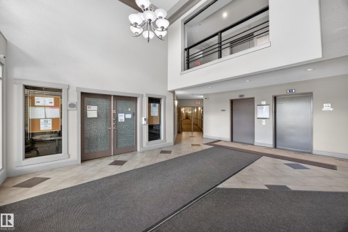 Spacious lobby featuring a high ceiling, two elevators, tile flooring, and a second-story interior balcony with metal railings - 138 16035 132 Street, Edmonton, AB 
