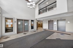 Spacious lobby featuring a high ceiling, two elevators, tile flooring, and a second-story interior balcony with metal railings - 
