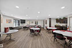 Spacious common area featuring wood-finish flooring, recessed lighting, and a full kitchen with dark cabinetry and black appliances - 