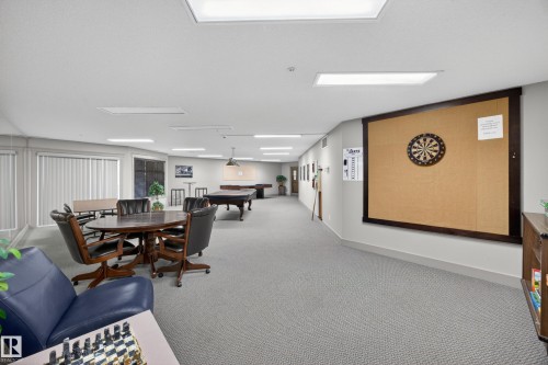 Spacious recreational room featuring gray patterned carpeting, recessed lighting, and a dartboard with a cork surround - 138 16035 132 Street, Edmonton, AB 