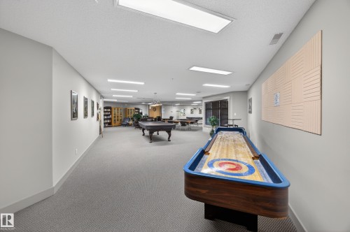 Spacious recreational room featuring a shuffleboard table, a billiard table, extensive built-in shelving, ample recessed lighting, and large windows - 138 16035 132 Street, Edmonton, AB 