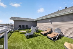 Expansive rooftop deck featuring artificial turf, a white railing with glass panels, and exterior wall lighting - 