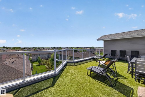 Expansive rooftop deck featuring artificial turf, clear glass railings, and a partial exterior wall with horizontal siding - 138 16035 132 Street, Edmonton, AB 
