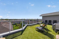 Expansive rooftop deck featuring artificial turf, clear glass railings, and a partial exterior wall with horizontal siding - 