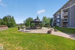 Outdoor common area featuring a central gazebo with seating, surrounded by a concrete patio and manicured lawn - 