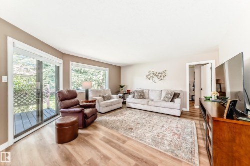 Living area featuring wood-finish flooring, a glass sliding door, and a large window overlooking trees - 10822 11 Avenue, Edmonton, AB 
