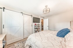 Double barn doors with black hardware, ceiling-mounted light fixture with industrial design, light-toned wall paint, and wood-finish flooring - 