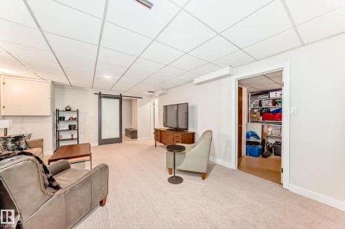 Carpeted room featuring a drop ceiling, white walls, and a sliding barn door with frosted glass - 10822 11 Avenue, Edmonton, AB 