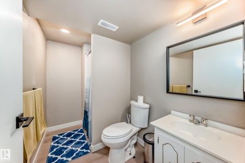 Bathroom featuring a white vanity with integrated sink, a rectangular framed mirror, modern wall-mounted lighting, and wood-finish flooring - 10822 11 Avenue, Edmonton, AB 