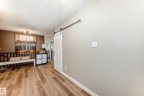 Wood-finish flooring throughout, featuring a white barn door on a black metal track and light gray wall paint - 10822 11 Avenue, Edmonton, AB 