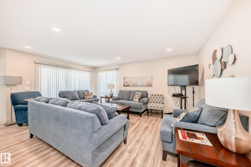 Spacious living area featuring light wood-finish flooring, recessed lighting, and expansive windows with vertical blinds - 10822 11 Avenue, Edmonton, AB 