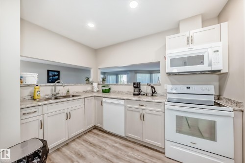 Modern kitchen featuring white cabinetry, light-toned countertops, a white electric range, and an over-the-range microwave - 10822 11 Avenue, Edmonton, AB 
