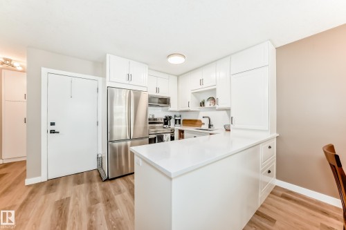 Contemporary kitchen featuring white cabinetry, stainless steel appliances, a white solid surface countertop, and wood-finish flooring - 10822 11 Avenue, Edmonton, AB 