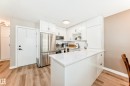 Contemporary kitchen featuring white cabinetry, stainless steel appliances, a white solid surface countertop, and wood-finish flooring - 10822 11 Avenue, Edmonton, AB 