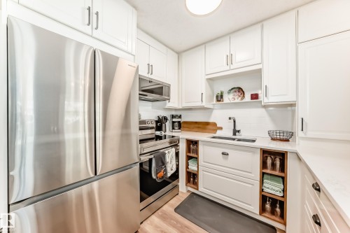 Contemporary kitchen featuring stainless steel appliances, white cabinetry with modern hardware, and wood-finish flooring - 10822 11 Avenue, Edmonton, AB 