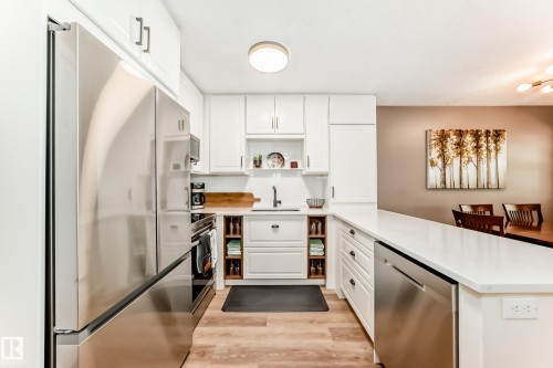 Modern kitchen featuring white cabinetry, stainless steel appliances, light wood-finish flooring, and white countertops - 10822 11 Avenue, Edmonton, AB 