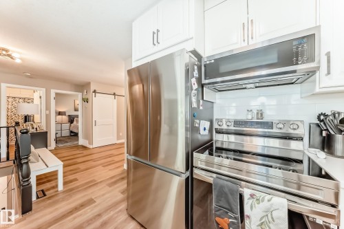 Kitchen area featuring white cabinetry, stainless steel appliances, a white subway tile backsplash, and wood-finish flooring - 10822 11 Avenue, Edmonton, AB 