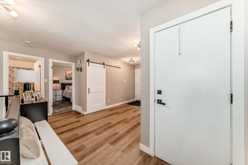 Entryway featuring a white solid-core door with black hardware, wood-finish flooring, light neutral wall paint, and a modern ceiling light fixture - 10822 11 Avenue, Edmonton, AB 