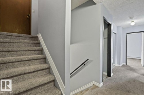 Carpeted stairs with a white handrail, leading to a hallway with light gray walls and a built-in closet - #1 13450 Fort Rd Nw, Edmonton, AB - Indoor Photo Showing Other Room