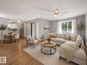 Open-concept living space featuring wood-finish flooring, light gray walls, a window with sheer white curtains, and a ceiling fan with integrated lighting - 1 13450 Fort Road, Edmonton, AB 