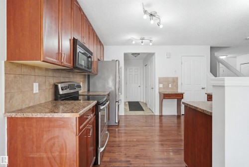 Kitchen featuring wood-finish flooring, rich wood cabinetry, stainless steel appliances, and a tiled backsplash - 1560 37B Avenue, Edmonton, AB 