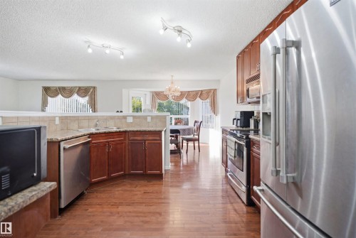 Kitchen featuring wood-finish flooring, stainless steel appliances, granite-look countertops, and rich wood cabinetry - 1560 37B Avenue, Edmonton, AB 