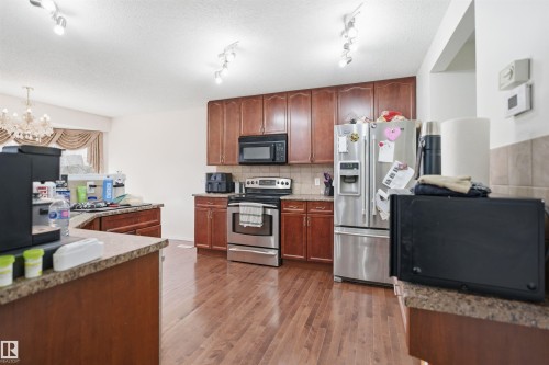 Kitchen featuring wood-finish flooring, rich wood cabinetry, stone-look countertops, and stainless steel appliances - 1560 37B Avenue, Edmonton, AB 