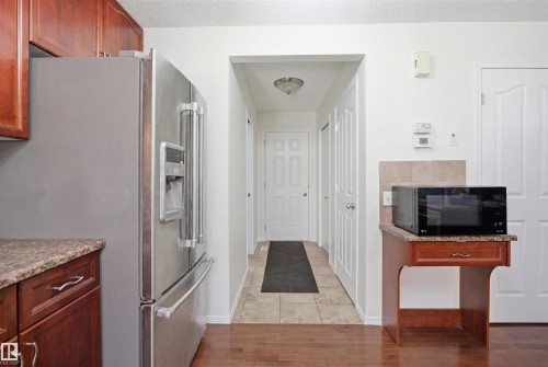 Kitchen area featuring rich wood cabinetry, a stainless steel refrigerator, and wood-finish flooring - 1560 37B Avenue, Edmonton, AB 