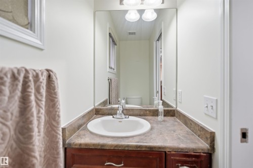 Bathroom vanity with a composite countertop, integrated white sink, chrome faucet, and a large wall-mounted mirror - 1560 37B Avenue, Edmonton, AB 