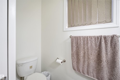 White toilet with a window featuring vertical blinds, a towel bar, and a toilet paper holder - 1560 37B Avenue, Edmonton, AB 