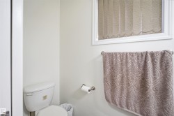 White toilet with a window featuring vertical blinds, a towel bar, and a toilet paper holder - 