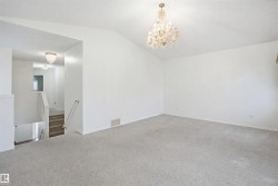 Spacious room featuring vaulted ceilings, a decorative chandelier, and light-toned carpeting - 