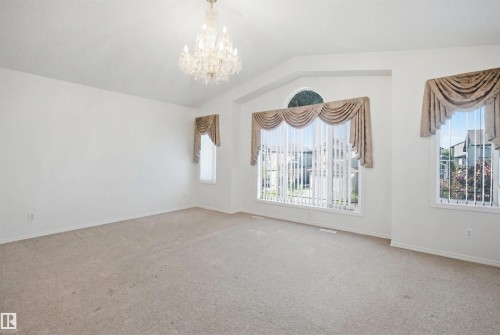 Spacious room featuring vaulted ceilings, a prominent chandelier, multiple large windows with vertical blinds and valances, and light-toned carpeting - 1560 37B Avenue, Edmonton, AB 