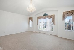 Spacious room featuring vaulted ceilings, a prominent chandelier, multiple large windows with vertical blinds and valances, and light-toned carpeting - 