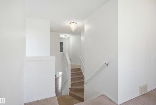 Carpeted staircase featuring a white painted handrail and a crystal-style flush mount light fixture - 1560 37B Avenue, Edmonton, AB 