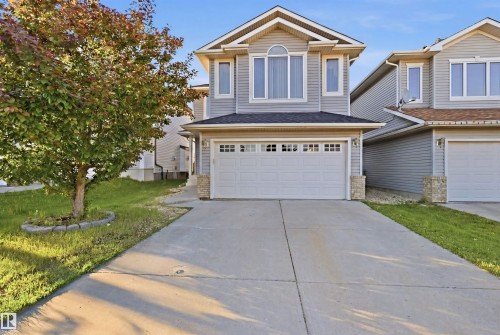 Two-story residential exterior featuring light gray siding, a prominent arched window, and a two-car garage with transom-style windows - 1560 37B Avenue, Edmonton, AB 
