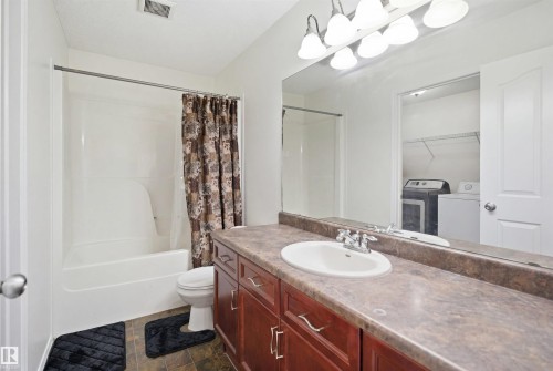 Full bathroom featuring a white tub and shower combination, a single vanity with wood-finish cabinetry, a laminate countertop, and an integrated sink with chrome fixtures - 1560 37B Avenue, Edmonton, AB 