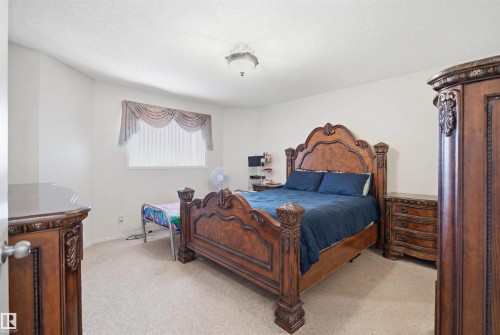 Spacious bedroom featuring light-toned carpeting, white walls, a white ceiling, and a single window with blinds and a decorative valance - 1560 37B Avenue, Edmonton, AB 