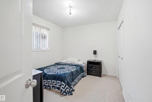 Bright interior room featuring a window with blinds, light-colored carpeting, white walls, and a built-in closet with bifold doors - 1560 37B Avenue, Edmonton, AB 