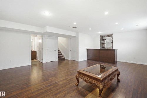 Spacious recreation room featuring wood-finish flooring, recessed lighting, and a built-in wet bar with a stone accent wall and shelving - 1560 37B Avenue, Edmonton, AB 