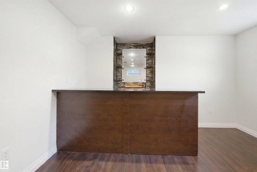 Built-in bar featuring a dark wood-finish base, a dark countertop, and a stacked stone backsplash with an integrated mirror - 1560 37B Avenue, Edmonton, AB 