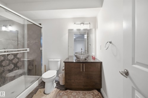 Bathroom featuring a glass-enclosed shower, a vanity with a vessel sink, dark wood-finish cabinetry, and a wall-mounted mirror - 1560 37B Avenue, Edmonton, AB 