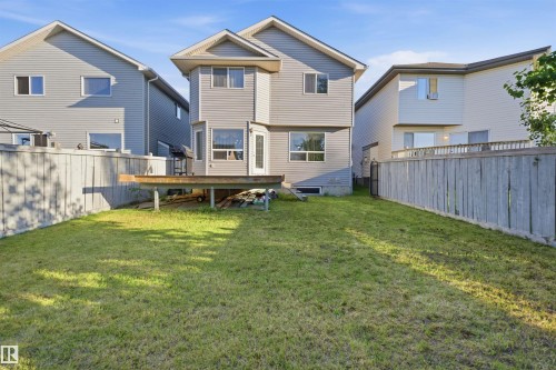 Fenced backyard featuring a wooden deck, mature lawn, and gray vinyl siding on the property's exterior - 1560 37B Avenue, Edmonton, AB 