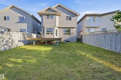 Fenced backyard featuring a wooden deck, mature lawn, and gray vinyl siding on the property's exterior - 